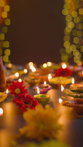 Vertical-Video-Close-Up-Shot-Of-Hands-Lighting-Diya-Oil-Lamps-Celebrating-Festival-Of-Diwali-On-Darkened-Table-1